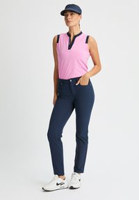 Różowa koszulka bez rękawów z granatowymi akcentami, połączona z dopasowanymi granatowymi spodniami. Model nosi białe trampki. Gładki materiał, minimalistyczny design.