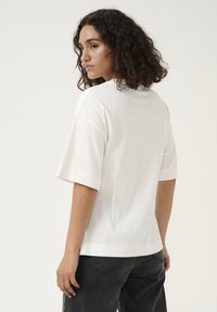 Korte mouwen witte t-shirt van zacht materiaal met een relaxte pasvorm, met een ronde halslijn en zijsplitten aan de onderkant. Gecombineerd met donkere jeans.