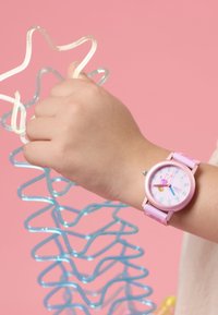 Roze polshorloge met een ronde wijzerplaat en een pastelband; beschikt over kleurrijke cijfers en een speels ontwerp; gecombineerd met kleurrijke plastic spiralen.