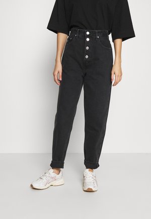 Jeans noirs taille haute avec un bouton-pression, jambe droite et ourlets retroussés. Assortis avec des baskets blanches présentant des accents roses subtils.