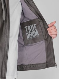 Brun läderjacka med grå foder; har en fyrkantig ficka med tryckknapp, märkt "TRUE DENIM" i fet stil.