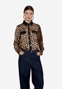 Camicia a bottoni con stampa leopardata, colletto e tasche nere, abbinata a jeans scuri a vita alta. Tessuto dalla superficie liscia.