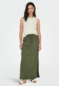 Wit geribbelde tanktop gecombineerd met een lange olijfgroene broekrok met trekkoord, voorzien van een zijsplit. Model draagt witte slidesandalen.