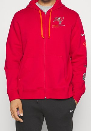 Sudadera con cremallera roja y cordones naranjas, logo de los Tampa Bay Buccaneers en el pecho y logotipos adicionales en las mangas. Tejido de mezcla de algodón.