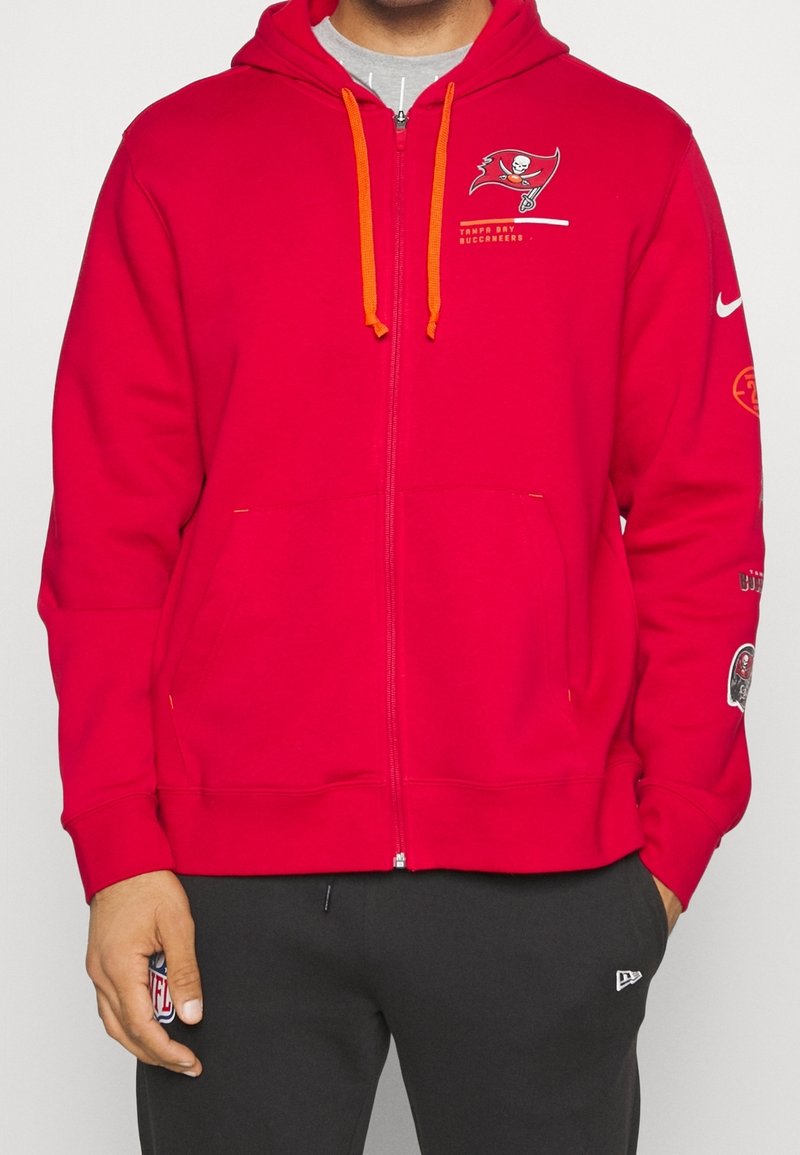 Rød zip-up hoodie med orange snore, Tampa Bay Buccaneers-logo på brystet og yderligere logoer på ærmerne. Blød blanding af bomuld.