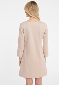 Beiges A-Linien-Kleid mit dreiviertel Ärmeln. Glattes, leichtes Material. Rundhalsausschnitt und umgeschlagene Ärmel. Minimalistisches Design, keine Muster oder Akzente.
