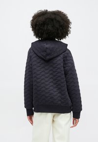 Czarny kaptur z pikowanym wzorem fali, z kapturem i ściągaczami, w połączeniu z jasnymi spodniami.