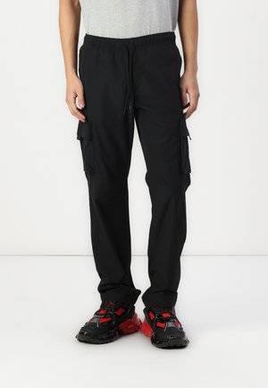 Black cargo pants with an elastic waistband, side pockets, and a loose fit, paired with black and red sneakers.
