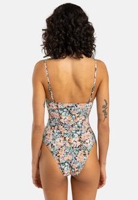 Blomsterbikini i ét stykke med tynde justerbare stropper, der har et flerfarvet blomstermotiv på en sort baggrund. Høj skæring, tætsiddende pasform.