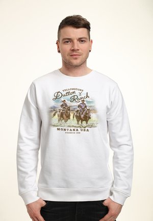 Homme portant un sweat-shirt blanc avec un graphisme de deux cow-boys à cheval et le texte "Yellowstone Dutton Ranch Montana USA Founded 1886."