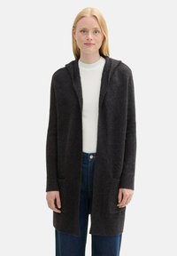 Mörkgrå huva cardigan gjord av ett texturerat stickat material med öppen fram, långa ärmar och två framfickor. Bärs över en vit topp och jeans.