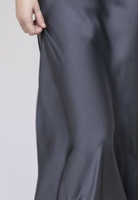 Jupe en satin gris foncé avec une texture lisse et brillante, présentant un design fluide qui tombe avec élégance à partir de la taille.