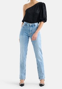 Schwarz, einseitig tragendes Oberteil mit strukturiertem Muster, kombiniert mit hellblauen, hoch taillierten Jeans und schwarzen, spitzen High Heels mit Schleifen Detail.