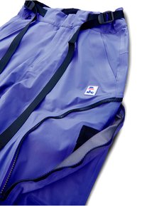 Pantalones cortavientos morados con correas ajustables negras, cremalleras y un parche con logo. Elaborados con una tela ligera y suave con acabado mate.
