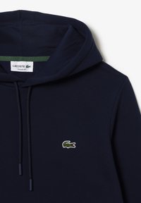 Felpa blu navy realizzata in morbido tessuto, con tasca a marsupio frontale, cappuccio regolabile con cordini e un piccolo logo di coccodrillo verde sul petto.