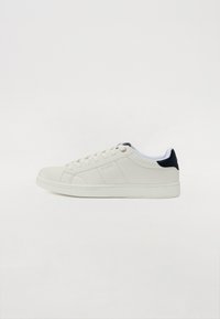 Hvit lær sneaker med rund tå, flat såle og marineblå aksent ved hælen. Har et snørelukking og subtilt sydd detaljering.