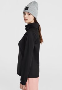 Svart långärmad topp med hög krage och ribbade manschetter, tillsammans med en ljusgrå stickad beanie med en logotyp. Mjuk tygstruktur.
