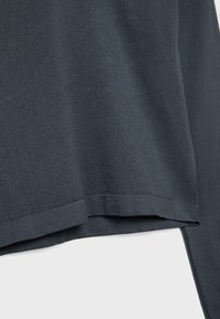Nahaufnahme eines dunkelgrauen Stoffes mit sichtbarem Saum und geschichteten Details am Rand, die eine glatte Textur und leichtes Drapieren zeigen.