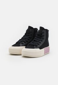 Czarne sneakersy typu high-top z teksturowanym wykończeniem zamszowym, kremową gumową podeszwą i fioletowym akcentem na pięcie. Płaskie sznurówki i naszywka z logo.