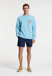 Light blue sweatshirt with graphic text on the chest, paired with navy blue shorts featuring a cactus pattern. Beige shoes.