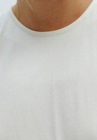 Gros plan sur une personne portant un t-shirt blanc uni à col rond, montrant le cou et la partie supérieure de la poitrine.