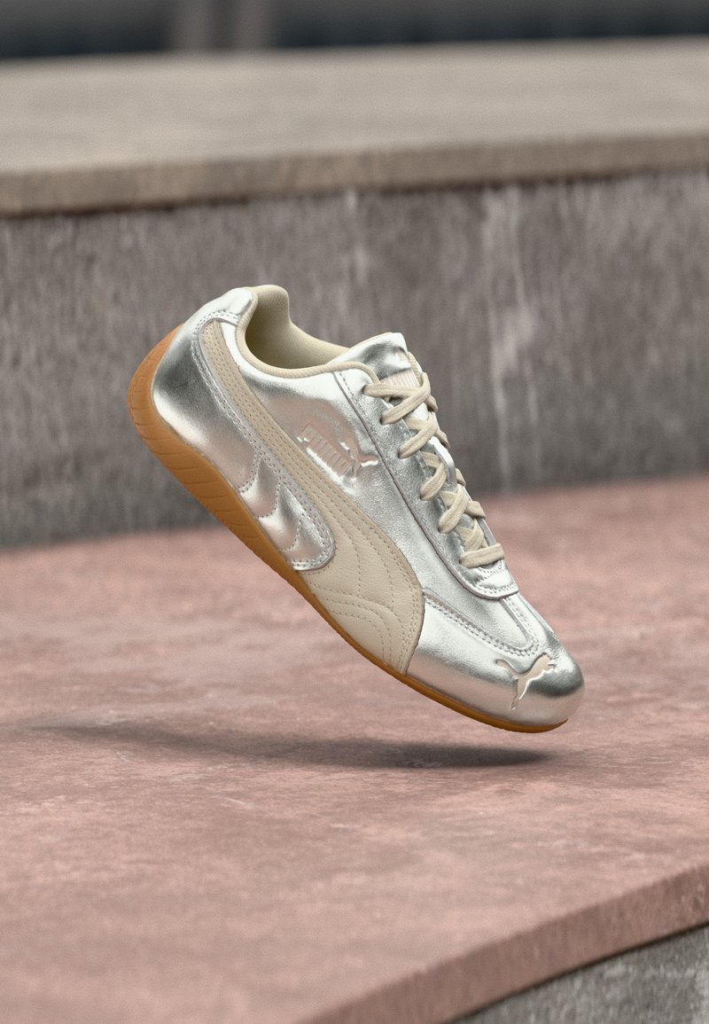 Baskets Puma argentées et beiges avec semelle en gomme, flottant au-dessus de marches en pierre roses et grises.