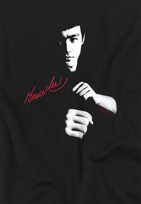 Black T-shirt featuring a stylized white print of a person in a fighting pose, with the text "Bruce Lee" in red script.