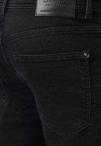 Czarne dżinsy z dzianiny mają wycięte kieszenie, obszyty pas i fakturowane wykończenie. Z tylu widoczna jest skórzana naszywka z logo.