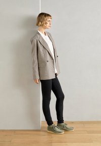 Blazer xadrez em castanho e branco, sobre uma camisa branca, combinado com jeans skinny pretos e sapatos de camurça verde com sola de borracha.