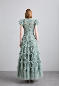 Robe vert menthe avec un corsage ajusté orné d'une broderie en forme de cœur, des manches courtes à volants et une jupe à volants superposés. Matériaux transparents et texturés.