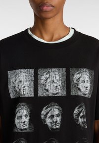 Camiseta negra con un estampado gráfico de bustos texturizados en escala de grises dispuestos en un patrón de cuadrícula. Cuello acanalado con una capa interior de color azul claro.
