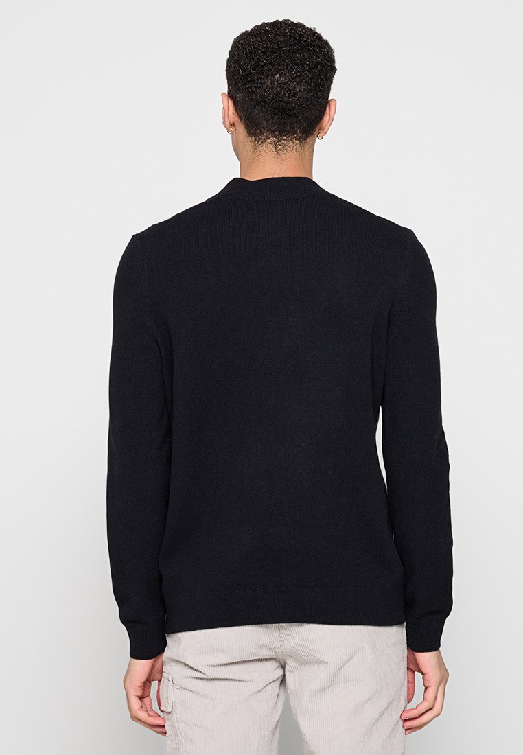 Schwarzer Strickpullover mit langen Ärmeln, rundem Ausschnitt und gerippten Bündchen, von hinten vor einem hellen Hintergrund gezeigt.