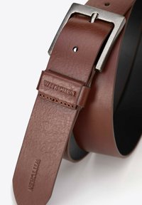 Bruine leren riem met een textuurafwerking, voorzien van een metalen zilveren gesp en het geperste "WITTCHEN"-logo nabij de gesp.