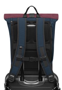 Sötétkék anyagú hátizsák, bordó tetővel. Párnázott hálós vállpántokkal, cipzáras zsebével és állítható csattal rendelkezik. Úgy tervezték, hogy könnyen a bőröndre rögzíthető legyen.