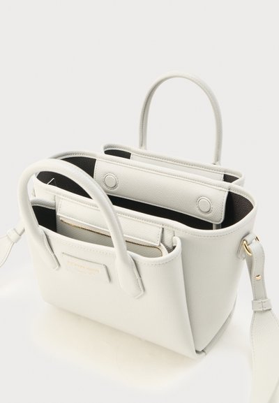 Λευκή δερμάτινη τσάντα χειρός με δύο λαβές, ανοιχτό επάνω μέρος με μαγνητικά κλείστρα, εσωτερική τσέπη με φερμουάρ και αφαιρούμενο ιμάντα ώμου με χρυσά εξαρτήματα.