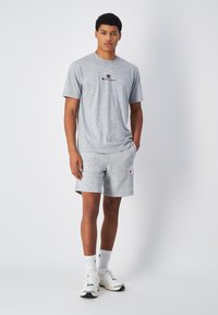 Grijze katoenen t-shirt en shorts met logo-accenten. T-shirt heeft een ronde hals, shorts hebben zakken en een elastische tailleband. Witte sneakers.