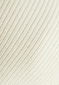 Jasnokremowa dzianina o fakturze i prążkowanym wzorze, z miękką, grubą włóczką, która nadaje głębię i wymiar.