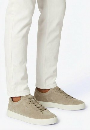 Sneakers beige in suede basse con suole bianche indossate con pantaloni a gamba dritta color avorio.