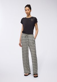 Maglietta nera con decorazioni floreali sulla spalla, abbinata a pantaloni a gamba larga a vita alta con un motivo di foglie in bianco e nero.