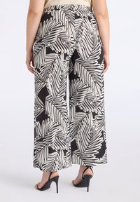 Zwarte wijde broek met een wit palmenbladpatroon. Elastische taille, lichtgewicht stof, gecombineerd met high-heeled sandalen voor extra lengte.