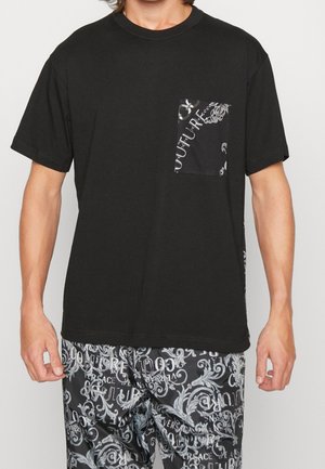 Una camiseta de algodón negra presenta un bolsillo con un patrón contrastante. Se combina con pantalones negros que exhiben un texto y un diseño blanquecinos ornamentales.