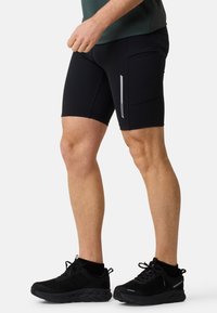 Shorts sportivi neri realizzati in tessuto elastico, dotati di tasca laterale, striscia riflettente e design aderente, abbinati a calzature nere.