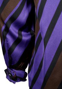 Tissu à manches longues rayé violet et marron avec des boutons noirs sur le poignet, présentant un détail froncé au niveau du poignet.