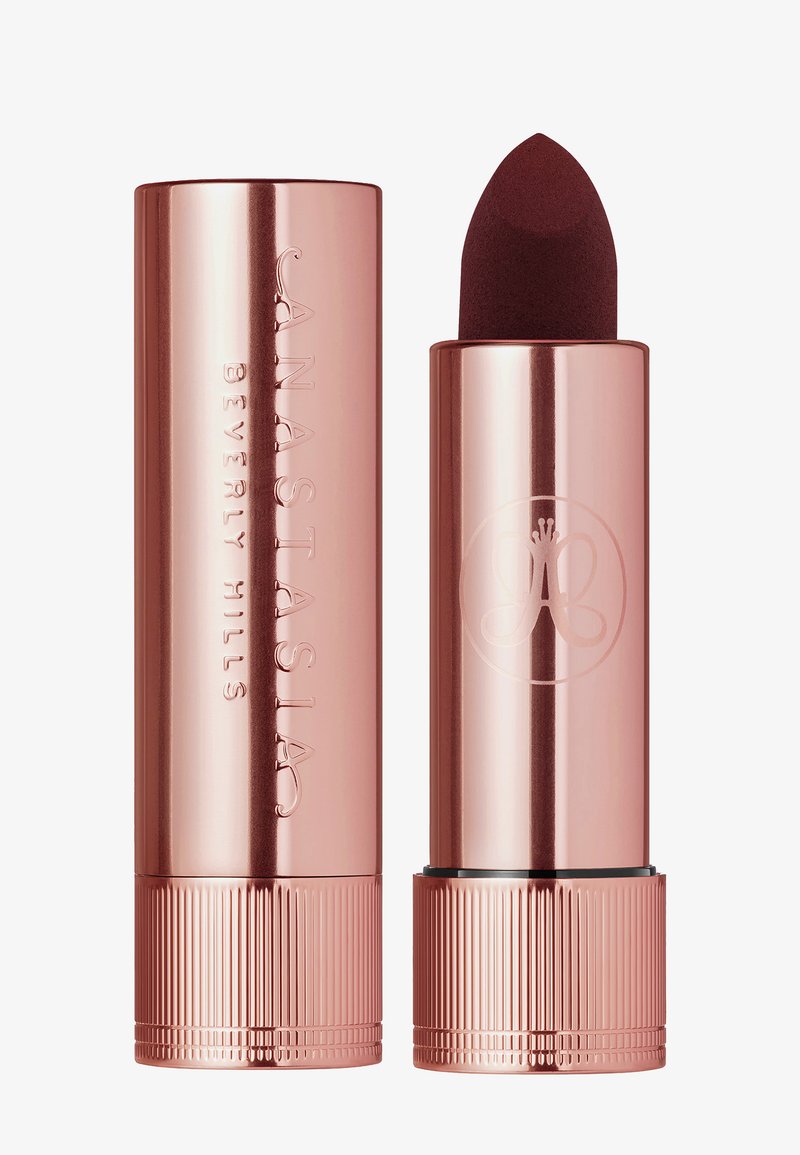Roze-gouden lippenstiftbuis met een afgeronde bovenkant, gegraveerd logo en een gestructureerde basis. De lippenstift heeft een diepe bordeauxrode tint.
