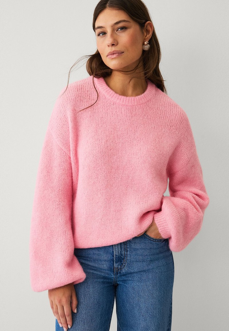 Maglione rosa realizzato in tessuto morbido e strutturato, con scollo rotondo e maniche oversize e voluminose, abbinato a jeans di denim blu.