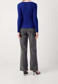 Haut à manches longues bleu côtelé avec un col rond plongeant, associé à un jean gris à jambes larges. Des sandales noires à talons complètent la tenue.