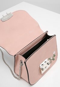 Borsa a mano in finta pelle rosa con dettagli in metallo argento, caratterizzata da un motivo floreale ricamato, tracolla a catena e scomparto aperto.