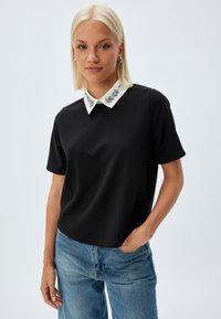 Zwarte top met korte mouwen en een witte kraag met versieringen. Gladde stof met een relaxte pasvorm en een iets ronde zoom.