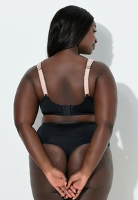 Sujetador negro con tirantes ajustables en tono nude y cierre de gancho y ojo. Braguita negra a juego de talle alto. Textura de tela suave y lisa.