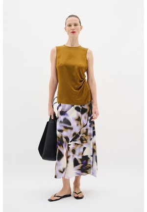 Satin-Top mit senfgelber Farbe und trägerlosem Design mit Drapierung; fließender knielanger Rock mit lila und schwarzen abstrakten Mustern; schwarze Tote-Tasche; Flip-Flops.